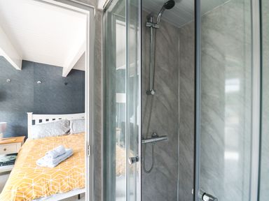 A bedroom with a bed and bedside tables next to a bathroom with a glass shower enclosure at Caban Glas in Llanafan near Pontrhydfendigaid