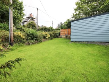 A grassy backyard with bushes and a blue shed near a wooden fence at Caban Glas in Llanafan near Pontrhydfendigaid
