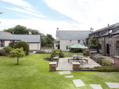 A garden with a patio table and umbrella surrounded by stone cottages at Honey Bee Cottage in Bradworthy
