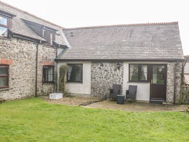 The exterior of a stone cottage with two chairs and a table on a small patio at Honey Bee Cottage in Bradworthy