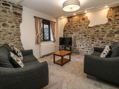 A living room with two grey sofas and a wooden coffee table in front of a stone wall with a television at Honey Bee Cottage in Bradworthy