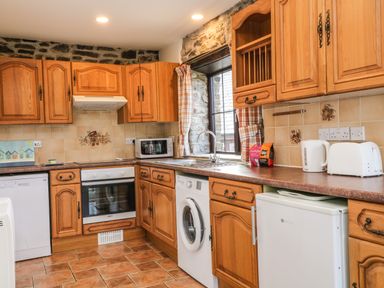 A kitchen with wooden cabinets a washing machine microwave oven toaster and kettle at Honey Bee Cottage in Bradworthy