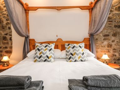A bedroom with a wooden canopy bed with patterned pillows and folded towels at Honey Bee Cottage in Bradworthy