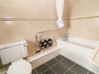 A bathroom with a toilet a towel rack a bathtub and a tiled wall at Honey Bee Cottage in Bradworthy