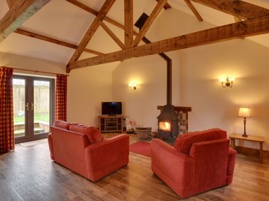 A living room with two red sofas a wood burning stove a tv and wooden beams at Woodpecker Cottage Bradworthy near Bude