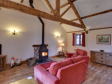 A sitting room with wooden beams red sofas a wood burner and wooden furniture at Woodpecker Cottage in Bradworthy near Bude