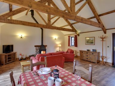 A living room with wooden beams a red sofa wood burning stove dining table with cups and plates at Woodpecker Cottage Bradworthy near Bude