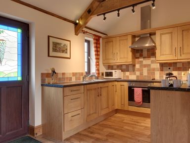 A kitchen with wooden cabinets a stove microwave and a stained glass door at Woodpecker Cottage in Bradworthy near Bude
