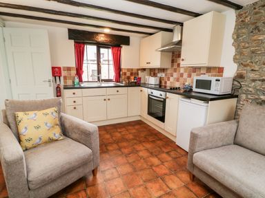 A kitchen with white cabinets two armchairs and a window with red curtains at Wagtail in Bradworthy near Bude