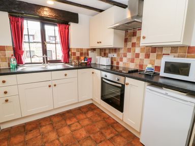 A kitchen with cabinets black countertops a sink oven microwave and window with red curtains at Wagtail in Bradworthy near Bude