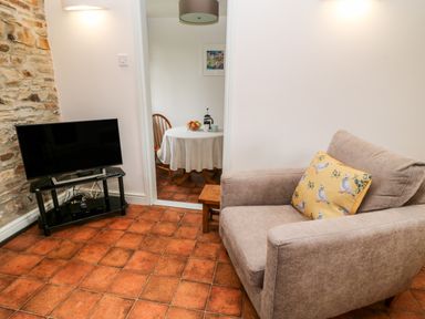 A living room with a chair and television on a stand next to a stone wall at Wagtail in Bradworthy near Bude
