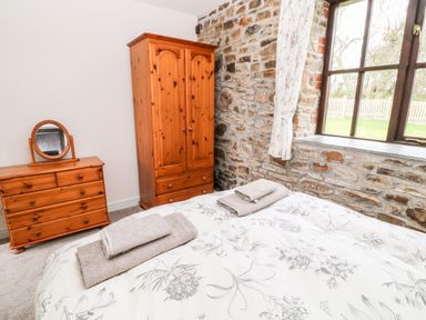 A bedroom with a wooden wardrobe and dresser a bed with towels and a stone wall with a window at Wagtail in Bradworthy near Bude