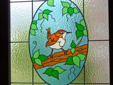 A stained glass window with a bird on a branch surrounded by leaves at Jenny Wren in Bradworthy