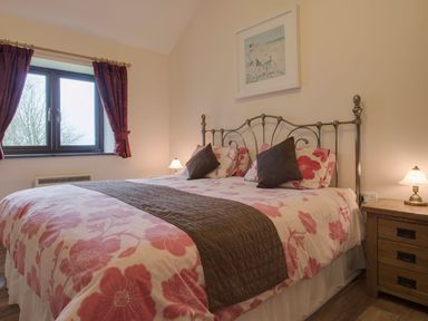 A bedroom with a bed with floral bedding two bedside tables with lamps and a window with curtains at Jenny Wren in Bradworthy