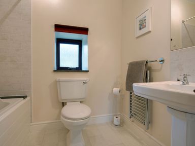 A bathroom with a toilet sink towel rail small window and part of a bathtub at Jenny Wren in Bradworthy
