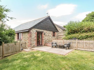 A stone house with wooden trim and a small fenced garden with a patio table and chairs at Jenny Wren in Bradworthy