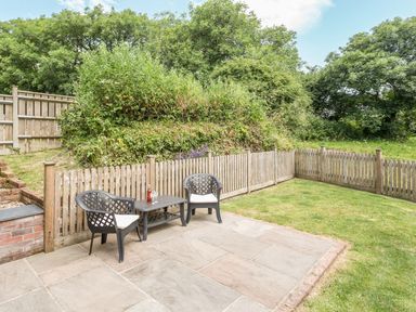 A patio with two chairs and a table next to a wooden fence and a garden at Jenny Wren in Bradworthy