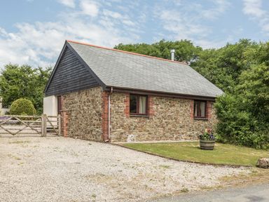 A stone cottage with a slate roof and two windows surrounded by trees and a gravel driveway at Jenny Wren in Bradworthy