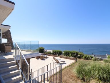 An outdoor terrace with lounge chairs and wicker furniture overlooking the sea at Boscregan in Porthleven