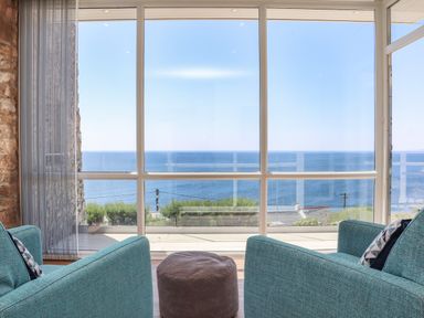 Two blue armchairs and a brown ottoman facing large windows overlooking the sea at Boscregan in Porthleven
