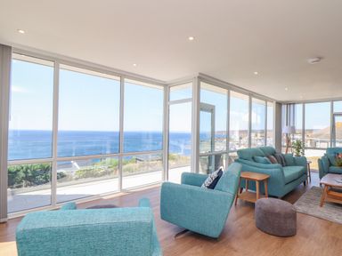 A living room with blue armchairs and sofas and large windows overlooking the sea at Boscregan in Porthleven