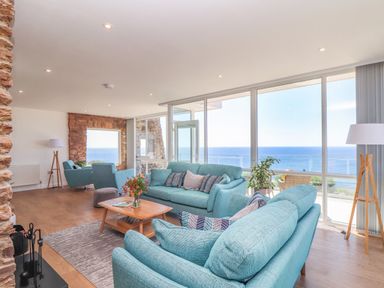 A living room with blue sofas a coffee table and large windows overlooking the sea at Boscregan in Porthleven