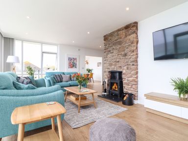 A living room with teal sofas a wooden coffee table a stone fireplace and a wall-mounted television at Boscregan in Porthleven