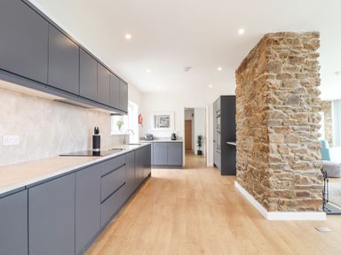 A kitchen with gray cabinets a stone wall and wooden floor at Boscregan in Porthleven