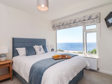 A bedroom with a bed facing a large window showing a sea view at Boscregan in Porthleven