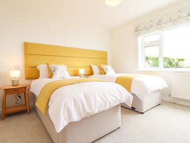 A bedroom with two single beds with yellow headboards and bedding beside a window at Boscregan in Porthleven