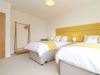 A bedroom with two single beds with yellow headboards beside a wooden clothing rack at Boscregan in Porthleven