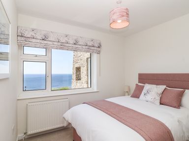 A bedroom with a bed near a window overlooking the sea at Boscregan in Porthleven
