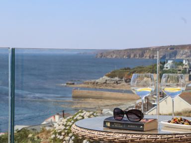 A glass table with two glasses of lemon water sunglasses and a book with a coastal view behind at Boscregan in Porthleven