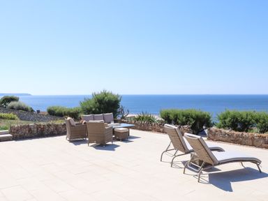 An outdoor patio with wicker furniture and loungers overlooking the sea at Boscregan in Porthleven