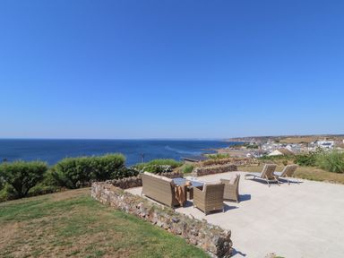 An outdoor patio with wicker seating and loungers overlooking the sea and coastal town at Boscregan in Porthleven