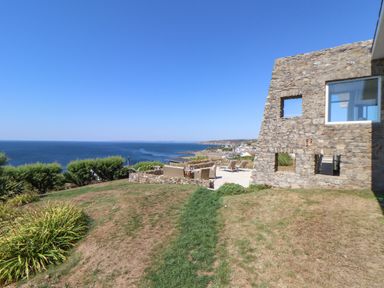 A stone building with square windows next to a patio with outdoor seating overlooking the sea at Boscregan in Porthleven