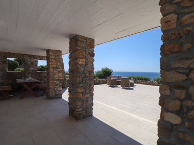 An outdoor patio with stone pillars a dining table with benches and a seating area overlooking the sea at Boscregan in Porthleven