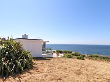 A white house with glass balcony by a grassy area overlooking the sea at Boscregan in Porthleven