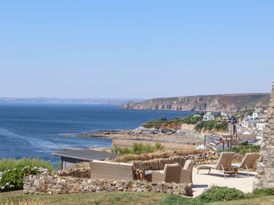 An outdoor patio with wicker furniture and reclining chairs overlooking the coastline and sea at Boscregan in Porthleven