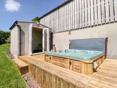 An outdoor wooden deck with a hot tub and an open door leading to a small room at Lovesome Pod in Lovesome Hill near Northallerton