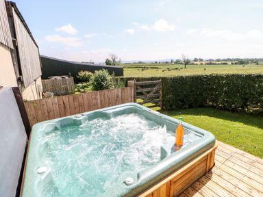 An outdoor hot tub with a bottle and two glasses on the edge overlooking a grassy field with cows at Lovesome Pod Lovesome Hill near Northallerton