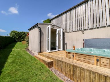 An outdoor wooden deck with a hot tub and open double doors leading into a building at Lovesome Pod Lovesome Hill near Northallerton