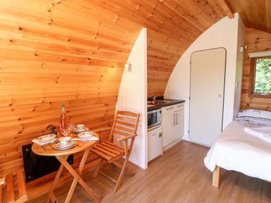 A small wooden room with a kitchenette a dining table with chairs and a bed at Lovesome Pod Lovesome Hill near Northallerton