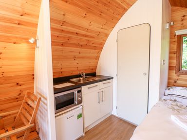 A small kitchenette with a microwave fridge and sink next to a door and a bed at Lovesome Pod Lovesome Hill near Northallerton