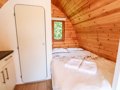 A small bedroom with a bed white linens folded towels a window and a closed door at Lovesome Pod Lovesome Hill near Northallerton