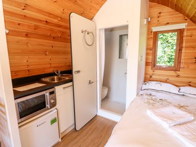 A wooden room with a small kitchenette a bed and an open bathroom door at Lovesome Pod Lovesome Hill near Northallerton