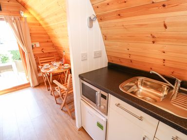 A small kitchenette with a sink microwave and fridge next to a dining table with wooden chairs and a bottle on the table at Lovesome Pod Lovesome Hill near Northallerton