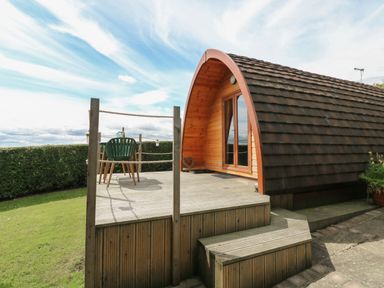 A wooden pod with a curved roof and a deck with a table and chair outside at Lovesome Pod Lovesome Hill near Northallerton