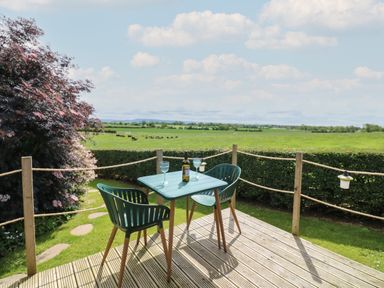 A deck with table and two chairs overlooking green fields and trees at Lovesome Pod Lovesome Hill near Northallerton