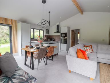 An open plan kitchen and living area with a dining table and chairs and a grey sofa with orange cushions at Pool View in Meifod Powys